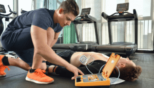 Man in an Adelaide gym uses a Mindray defibrillator on another person, lying on the floor, in a simulation of how to workplaces and buildings can be AED ready