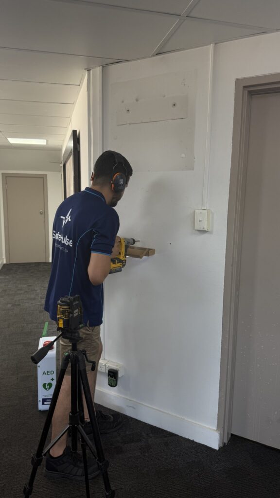 SafePulse technician installing an AED in a NSW commercial office hallway